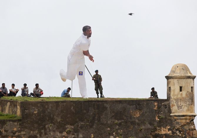 Spectators and soldiers, from behind a cut-out of Sri Lanka's Muttiah Muralitharan, watch cricket match between Sri Lanka and India in Galle