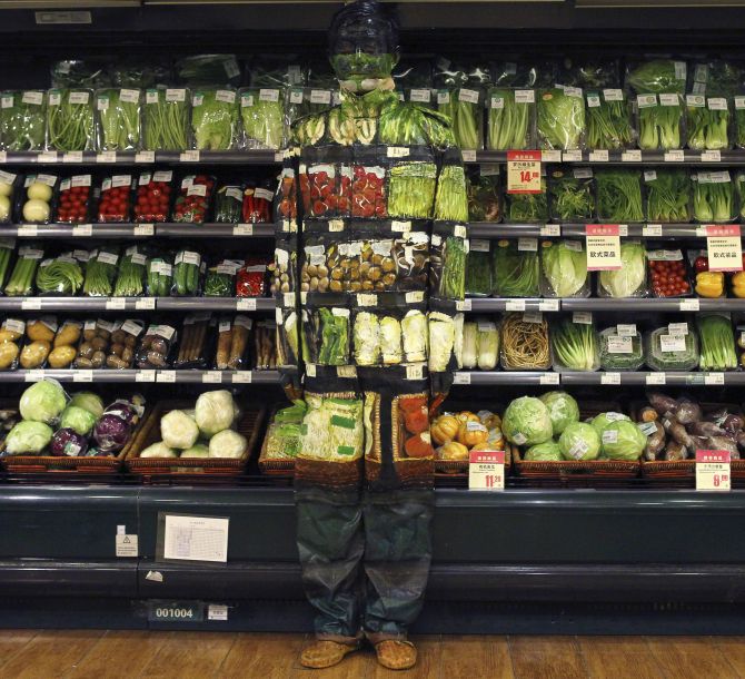 Artist Liu Bolin demonstrates an art installation by blending in with vegetables displayed on the shelves at a supermarket in Beijing